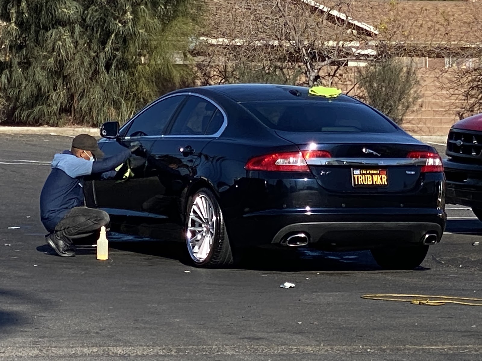 Worker hand-drying a black Jaguar sedan in the parking lot