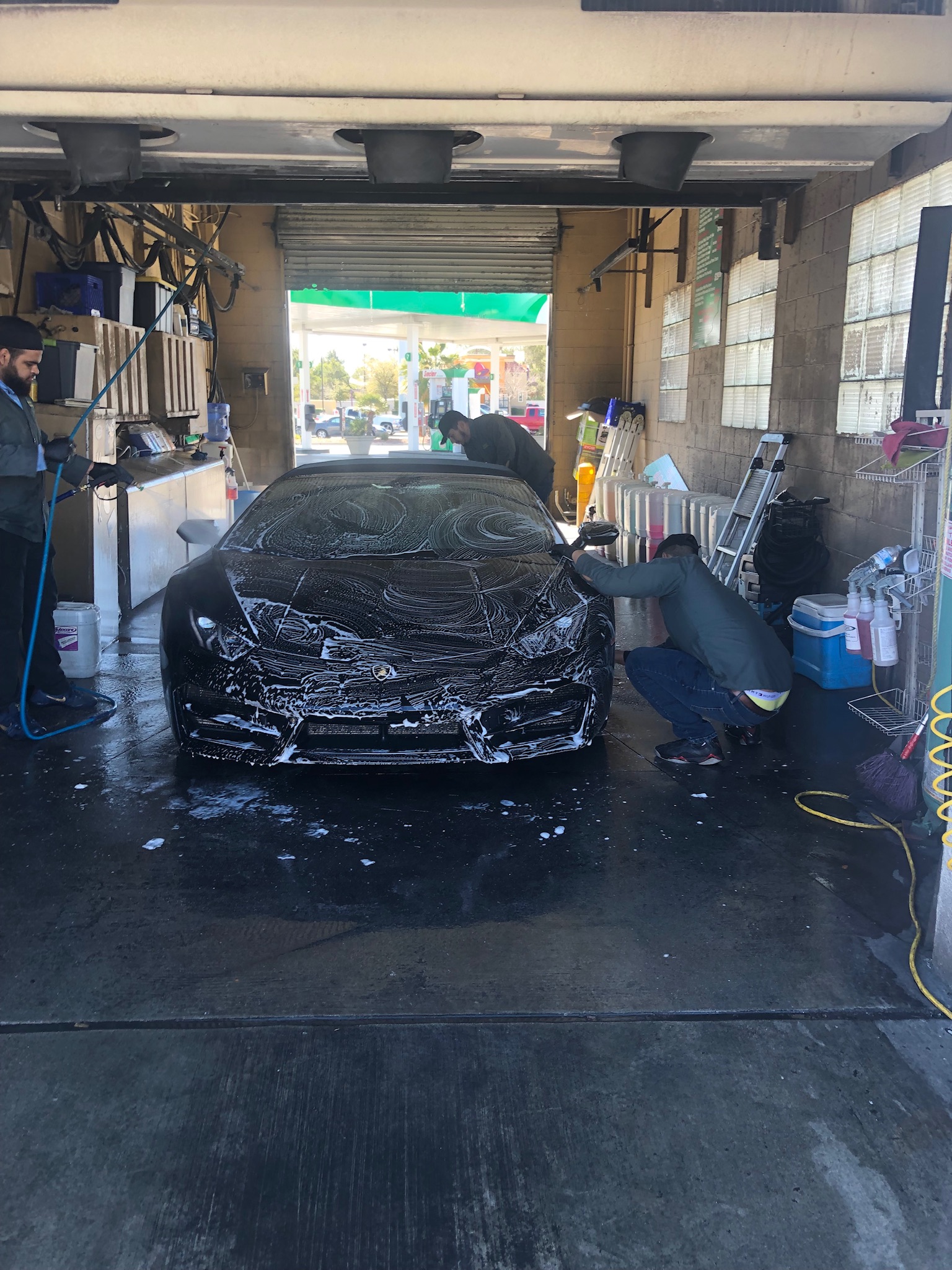 Crew hand-washing a soapy black Lamborghini inside the wash bay